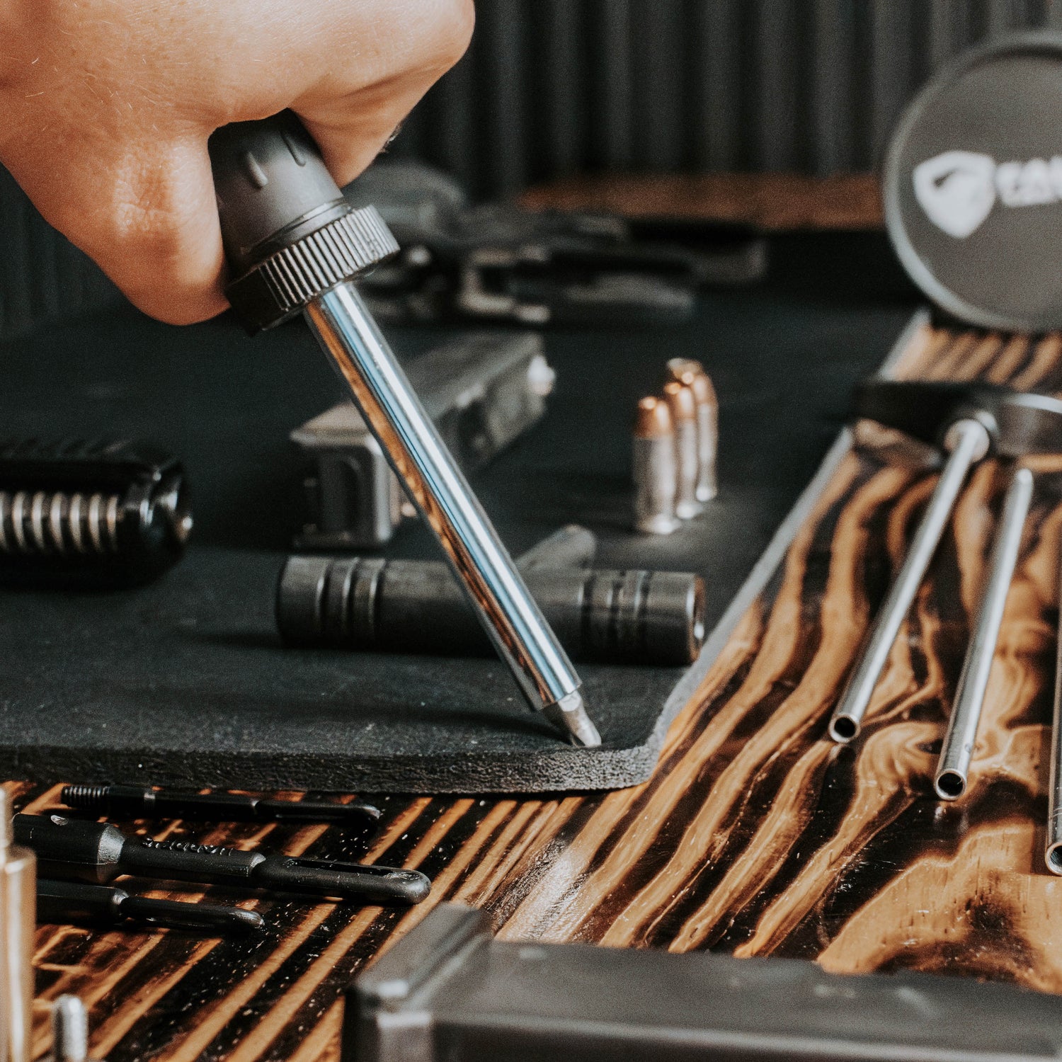 Hand using a tool on a wooden surface with various tools and equipment.