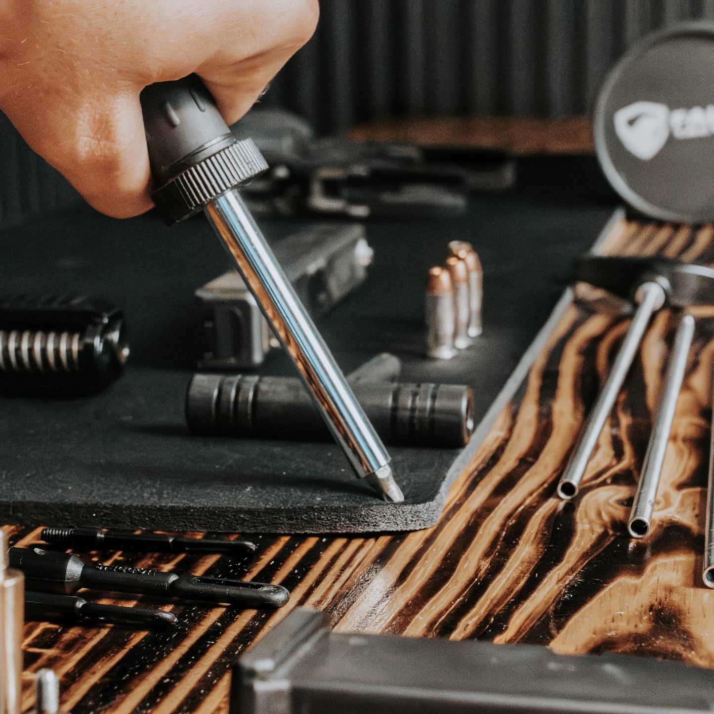 Hand using a tool on a wooden surface with various tools and equipment.