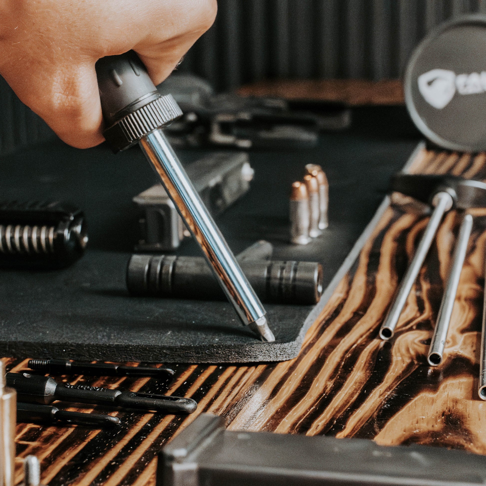Hand using a tool on a wooden surface with various tools and equipment.